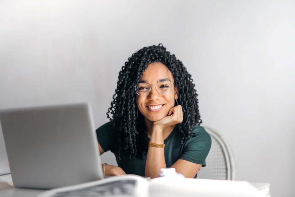 Happy Woman Sitting At Table With Laptop